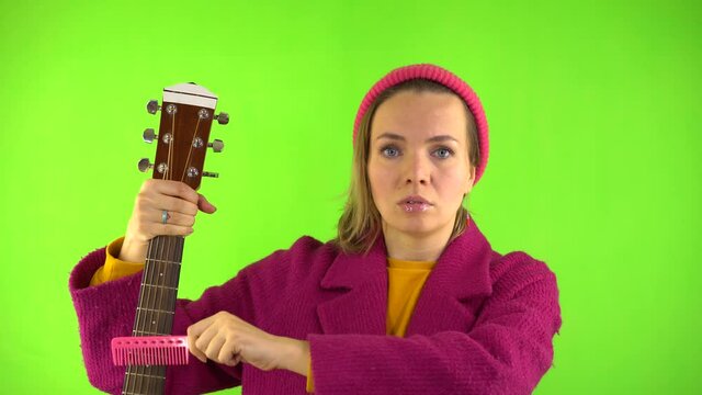 Crazy Woman with Strange Look, Pink Comb Combing Guitar, Surrealism on Green Background. Psychopath, Guitar Tuning, Advertising Concept.