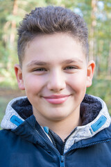 Straight on view of a young, smiling boy outside in the forest