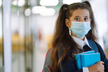 Schoolgirl in protective medical mask in school corridor. Protective measures against spreading of Covid-19 at school.