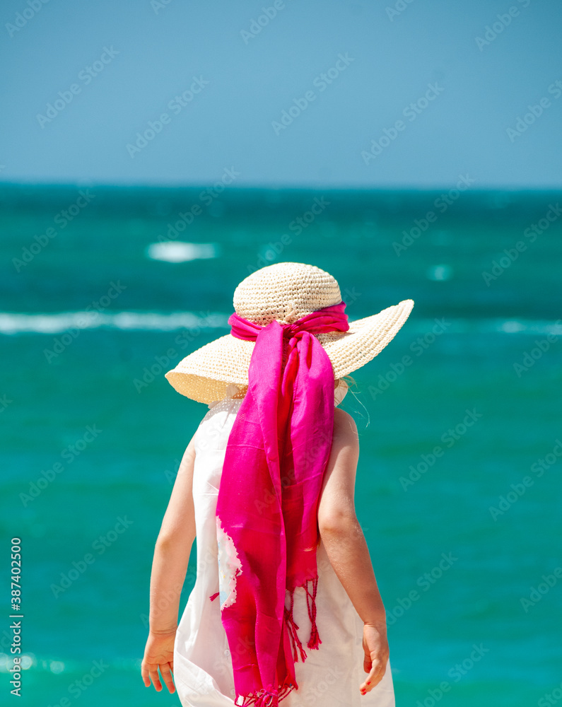 Wall mural holidays at the beach with tourqouise water of the ocean in the background a girl with a hat and a p