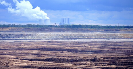 Braunkohle-Tagebau mit qualmenden Kühltürmen am Horizont 