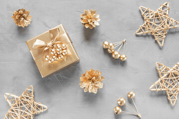 New Year's flat lay in golden and gray shades. Gift box, cones and berries are painted with golden paint. Stylish concept of christmas, celebration. Top view, minimalism, copy space.