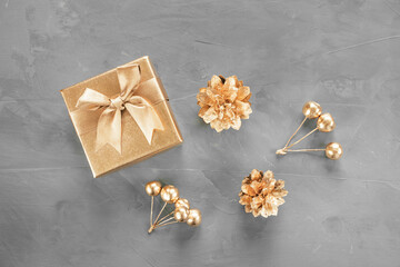 New Year's flat lay in golden and gray shades. Gift box, cones and berries are painted with golden paint. Stylish concept of christmas, celebration. Top view, minimalism, copy space.