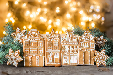 Christmas cookies gingerbread houses on wooden table with christmas lights in background, selective focus.