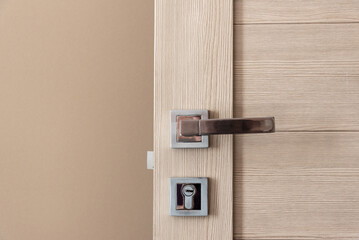 Close up stylish modern open wooden door with shiny silver and golden metal knob and lock near...