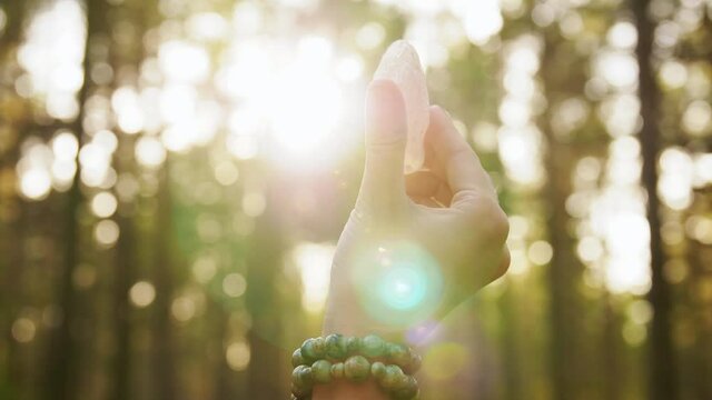 occult science and supernatural concept - hand of young woman or witch with semiprecious crystal or gemstone performing magic ritual in forest
