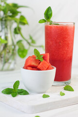 Buah Semangka or watermelon fruit, cut on wooden white chopping board, with a bowl of slices watermelon and watermelon juice. Bright mood photo on white marble background.