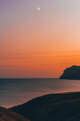 Amazing orange sunset on the sea with a view of mountains and hills, Crimea, Cape Chameleon. Sunset mountain landscape. 