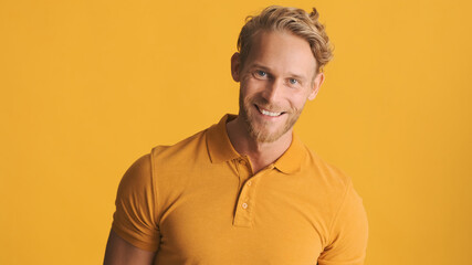 Handsome smiling bearded man looking happy spending time with friends isolated on yellow background. Joyful expression