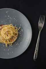 Traditional Italian dish spaghetti carbonara with bacon in a cream sauce in a plate over dark background. Top view with copy space. Served and ready to eat.