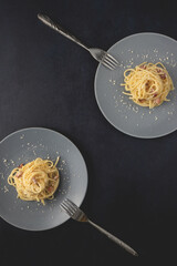 Two portions of Spaghetti traditional Italian dish spaghetti carbonara with bacon in a cream sauce in a plate over dark background. Top view with copy space.
