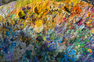 Stock Photo of a wooden painter palette with mixed and unmixed oil colours on sunlight. Concept art painter 