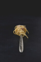 Fork of traditional Italian dish spaghetti carbonara isolated on dark background. Close-up view.