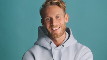 Attractive stylish bearded guy in hoodie joyfully posing on camera over colorful background. Positive expression