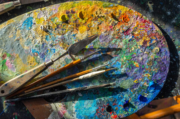 Stock Photo of a painter brushes and palette knife on a wooden palette with mixed and unmixed oil colours on sunlight. Concept art painter