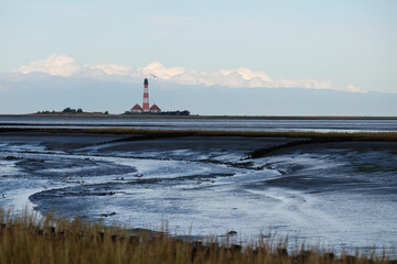 Fototapeta premium Ebbe in der Nordsee mit einem Leuchtturm in Westerhever/D im Hintergrund