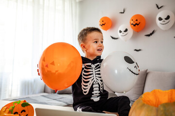 Little boy decorates the house for Halloween. Halloween boy in carnival costumes celebrating Halloween indoors. Cute little boy enjoying his halloween.