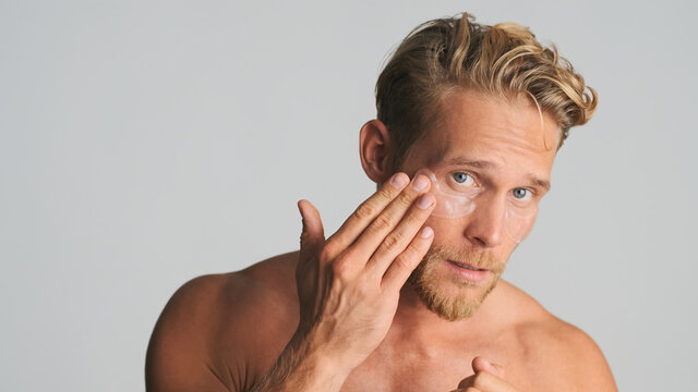 Handsome bearded man applying eye patches take care of his skin isolated on white background