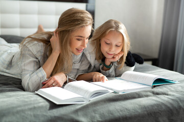 beautiful mom and daughter in pajamas lie in bed and read a book