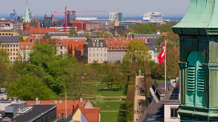 Beautiful panorama view over the historic center of Copenhagen, Denmark, with steeple, castle garden Kongens Have and avenue with pruned trees, flying Danish flag and the sea on the horizon.