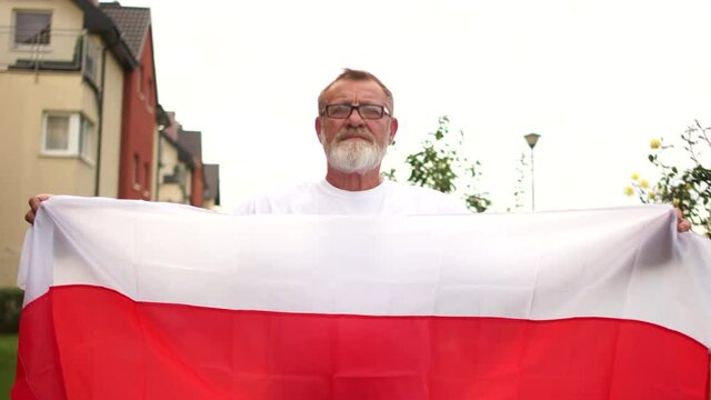 Close-up portrait of a gray-haired pensioner with glasses and a beard holding the red and white flag of Belarus. Protest in Belarus, color revolution
