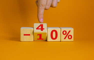 Hand turns a cube and changes the expression '-10 percent' to '-40 percent'. Beautiful orange background, copy space. Business concept.