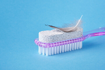 pumice stone with pink plastic handle and pedicure brush and bird feather on blue background, smooth skin of the foot