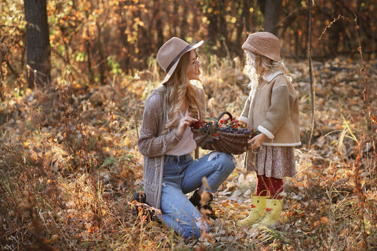 mom and daughter with a basket of berries in the woods on a walk in the fall