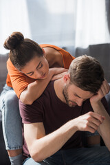 Obraz premium young woman leaning on back of depressed boyfriend sitting with bowed head