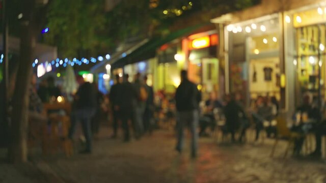 Evening street in the old town with numerous cafes and restaurants. People chat, eat and drink while sitting at cafe tables on summer terraces. Evening city illumination and comfort. Blurred out of