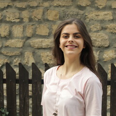 Young girl poses in front of a stone wall and a wooden fence