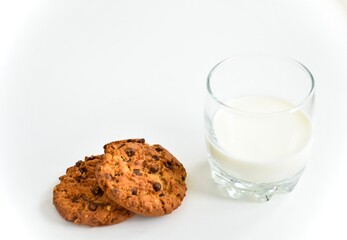 Oatmeal cookies with chocolate chips and a glass of milk on a white table.