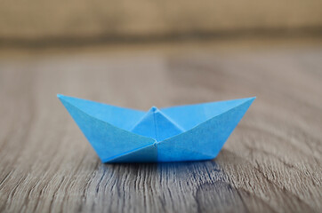 Obraz premium Origami blue paper boat isolated on woden background