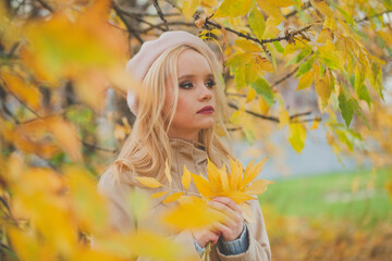 Beautiful blonde woman in fall park. Autumn woman with leaves in her hands on fall nature background