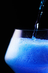 Naklejka na ściany i meble Blue drink is poured into a glass. Black background.