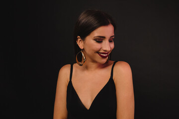 Happy Woman in black outfit smiling with closed eyes over black background . Charming lady in dark stylish dress has fun on isolated backdrop