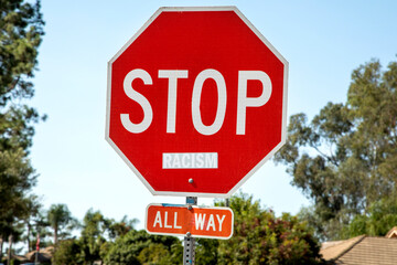 A stop sign with the word racism attached to the sign.