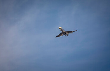 Private jet with landing gear down flying across blue sky with white cirrus clouds. Negative space is availalble.