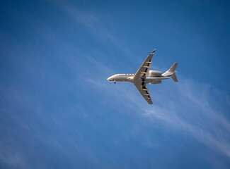 Private jet with landing gear down flying across blue sky with white cirrus clouds. Negative space is availalble.