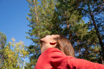 A girl with long hair in a red jacket is spinning against the background of tall trees in the forest. Bottom view