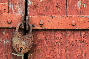 Locked old red double door with rusty padlock. Peeled door