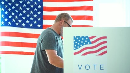 An elderly man with glasses and a gray beard votes at a polling station. Patriot during the 2020 us elections in the voting booth