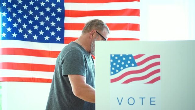 An elderly man with glasses and a gray beard votes at a polling station. Patriot during the 2020 us elections in the voting booth