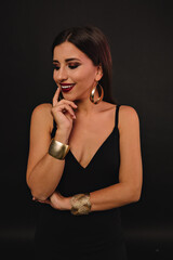 Obraz premium Exited smiling girl with golden jewerly dressed black outfit posing over black background