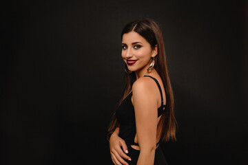 Naklejka premium Pretty woman with long hair wearing black outfit with jewelry in ears looking at camera over blackbackground