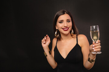 Happy exited woman dressed black dress with a glass of wine posing over black background. Holiday, birthday, New Year