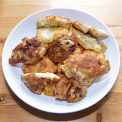Ready-made breaded chicken fillet on white plate on wooden background.
