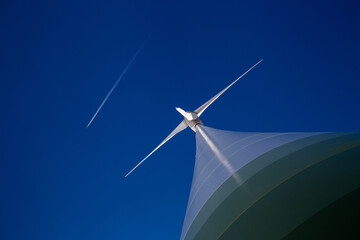 Huge wind turbine with blue sky and plane with contrail