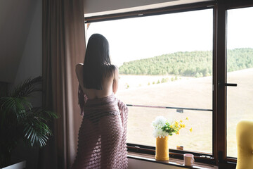 Semi naked woman wrapped in a shawl looking out through window