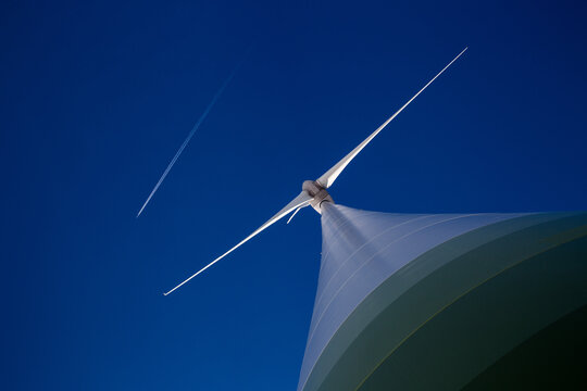 Huge wind turbine with blue sky and plane with contrail